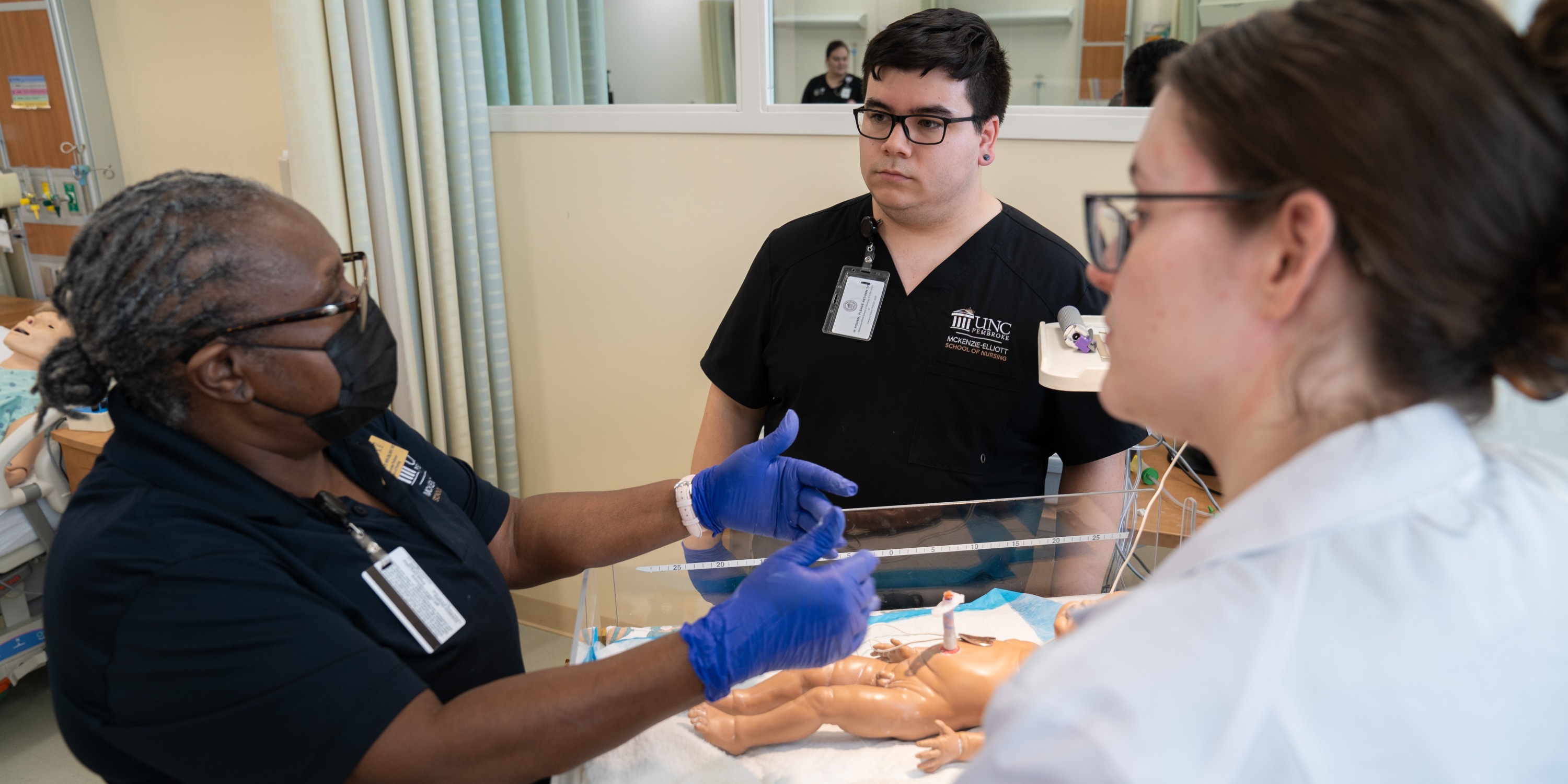 Nursing faculty instructing a male and a female nursing stuent in a newborn simulation lab at UNC Pembroke.