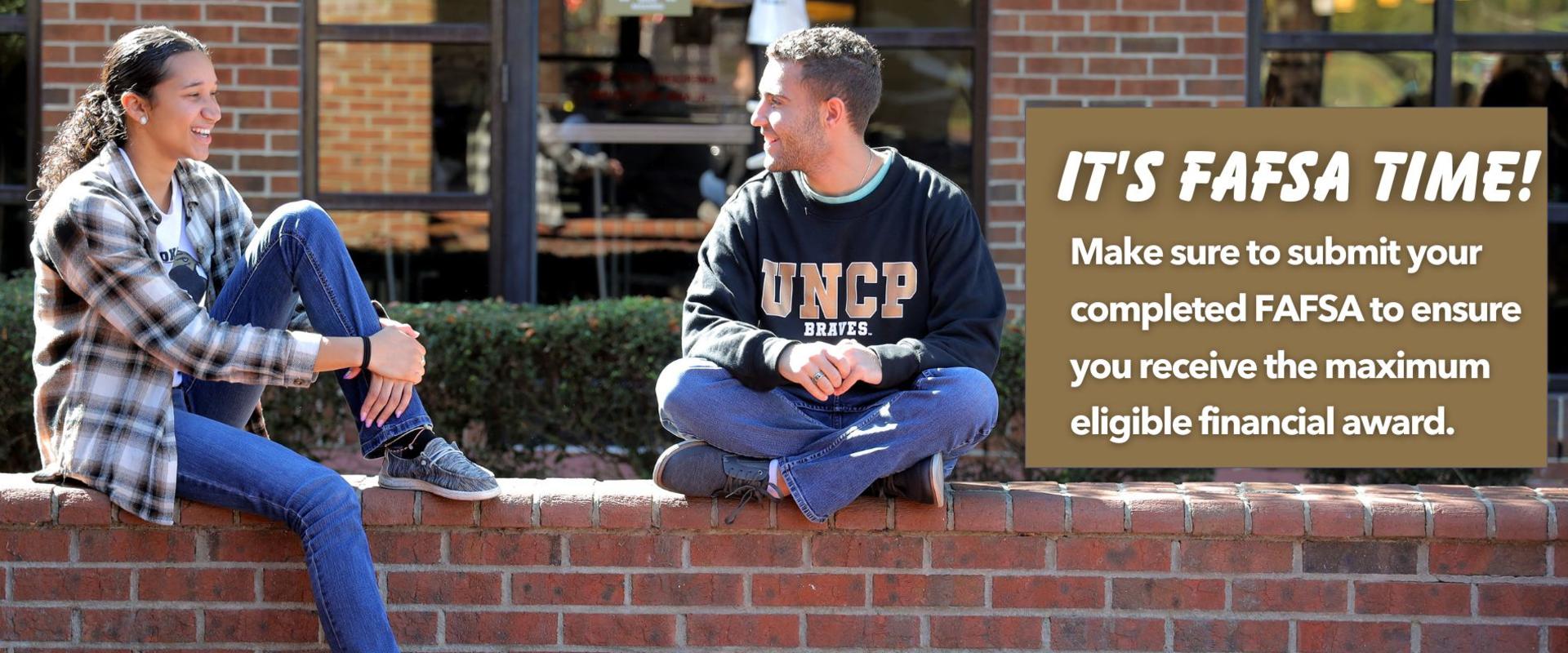 Two UNCP students sitting on a brick wall. 