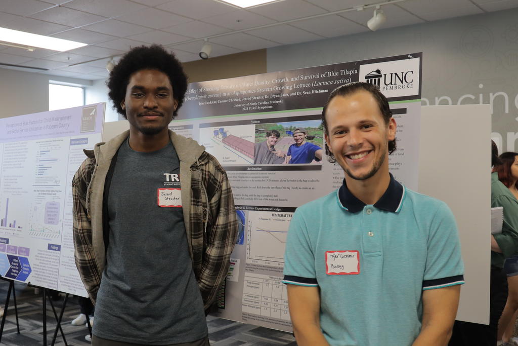 Jerrod Straiter (left) and Tyler Locklear pose in front of the poster "The Effects of Stocking Density on Water Quality, Growth and Survival of Blue Tilapia in an Aquaponies System Growing Lettuce