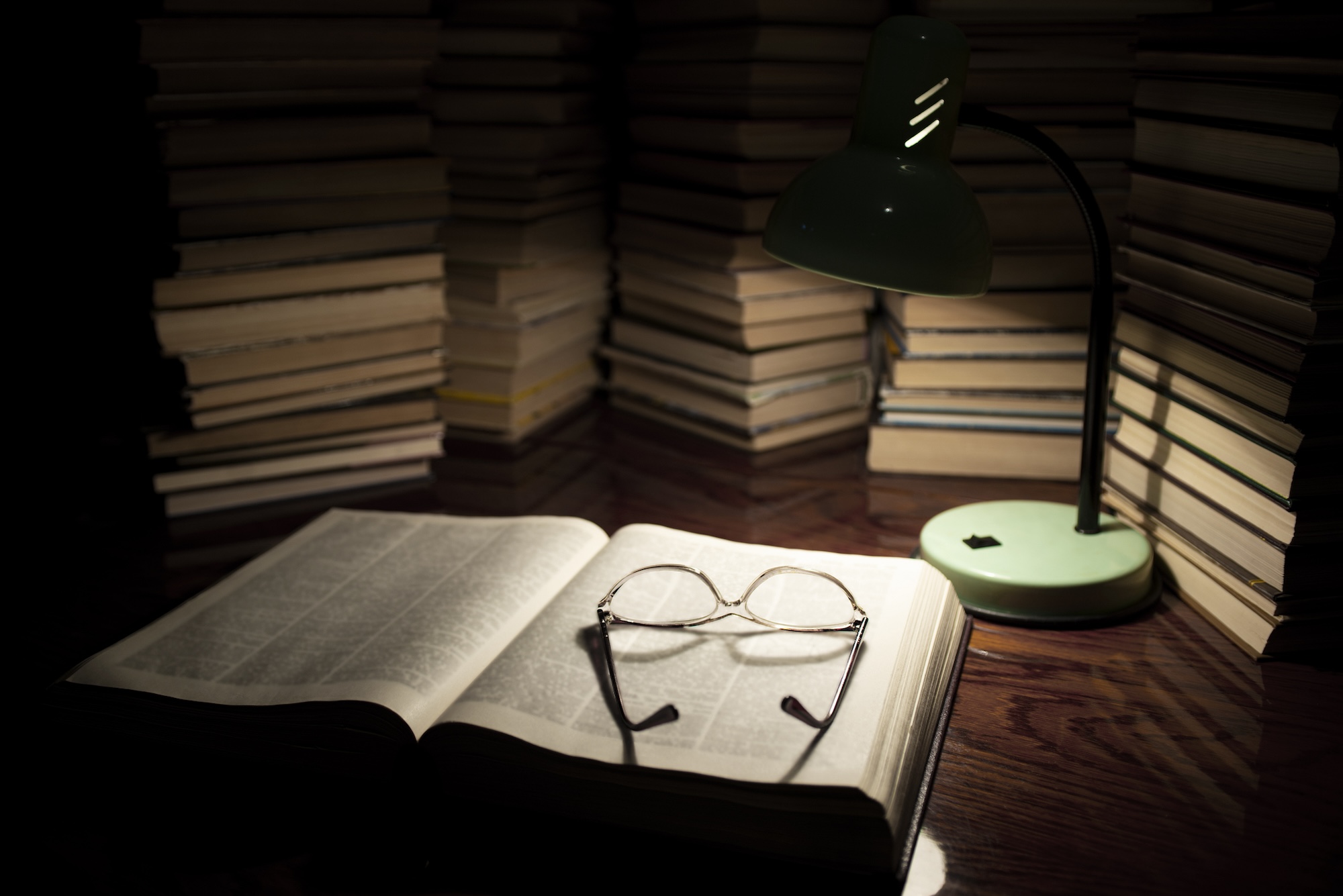 A pile of books behind one center book with glasses on it