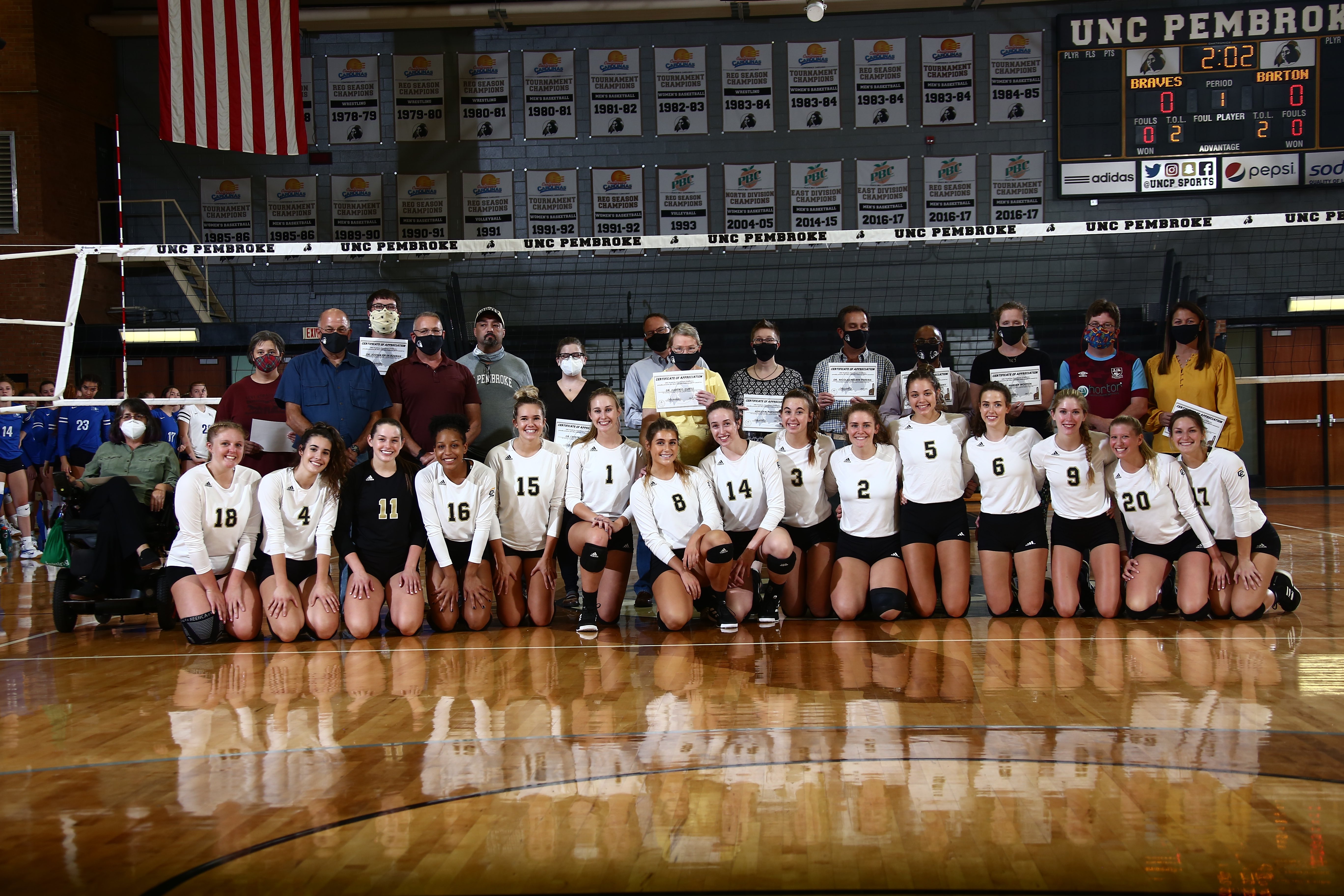 Volleyball team and their honored faculty and staff posing for a picture on the volleyball court