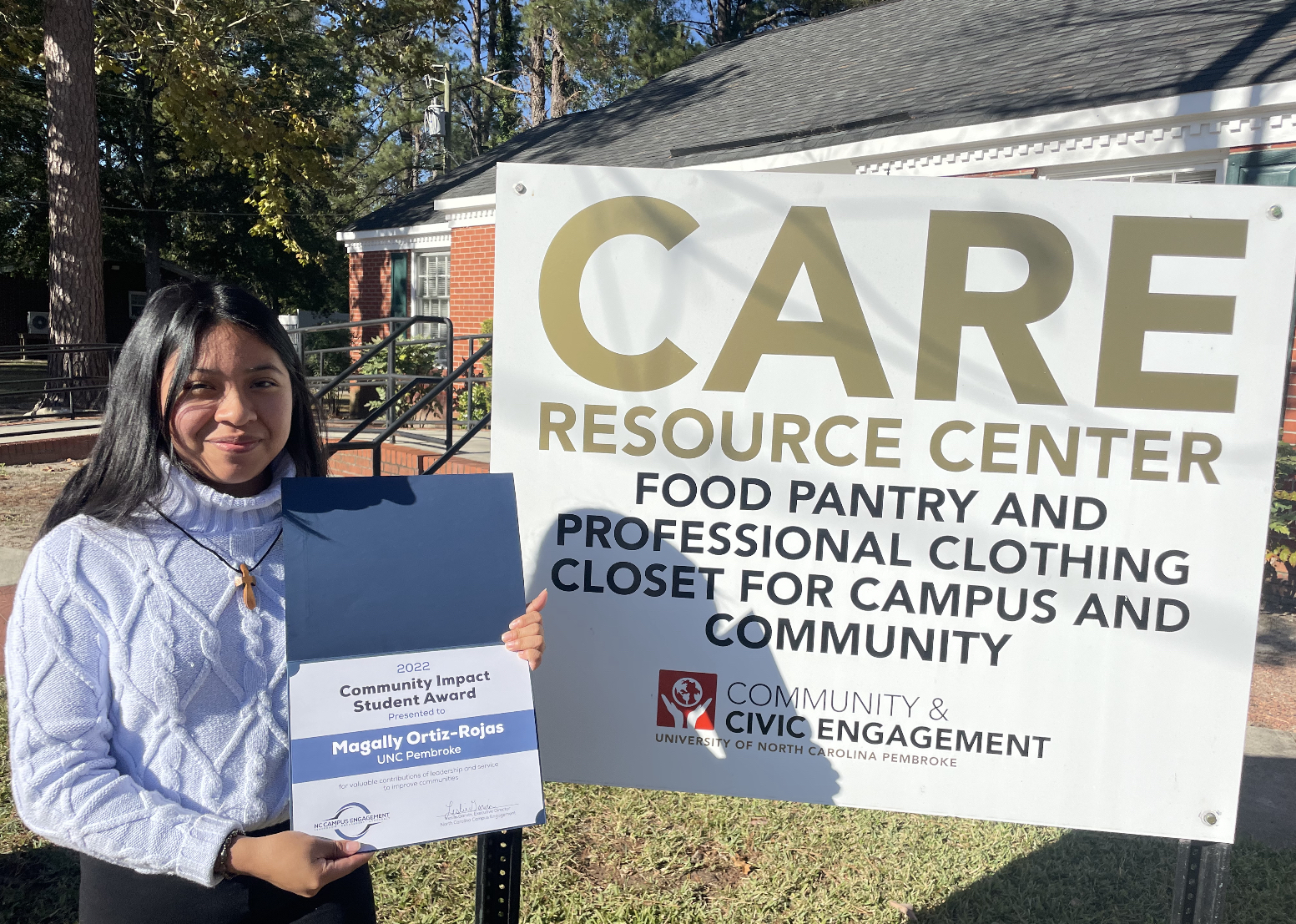 Ortiz standing in front of the CARE Resource Center sign holding a certificate 