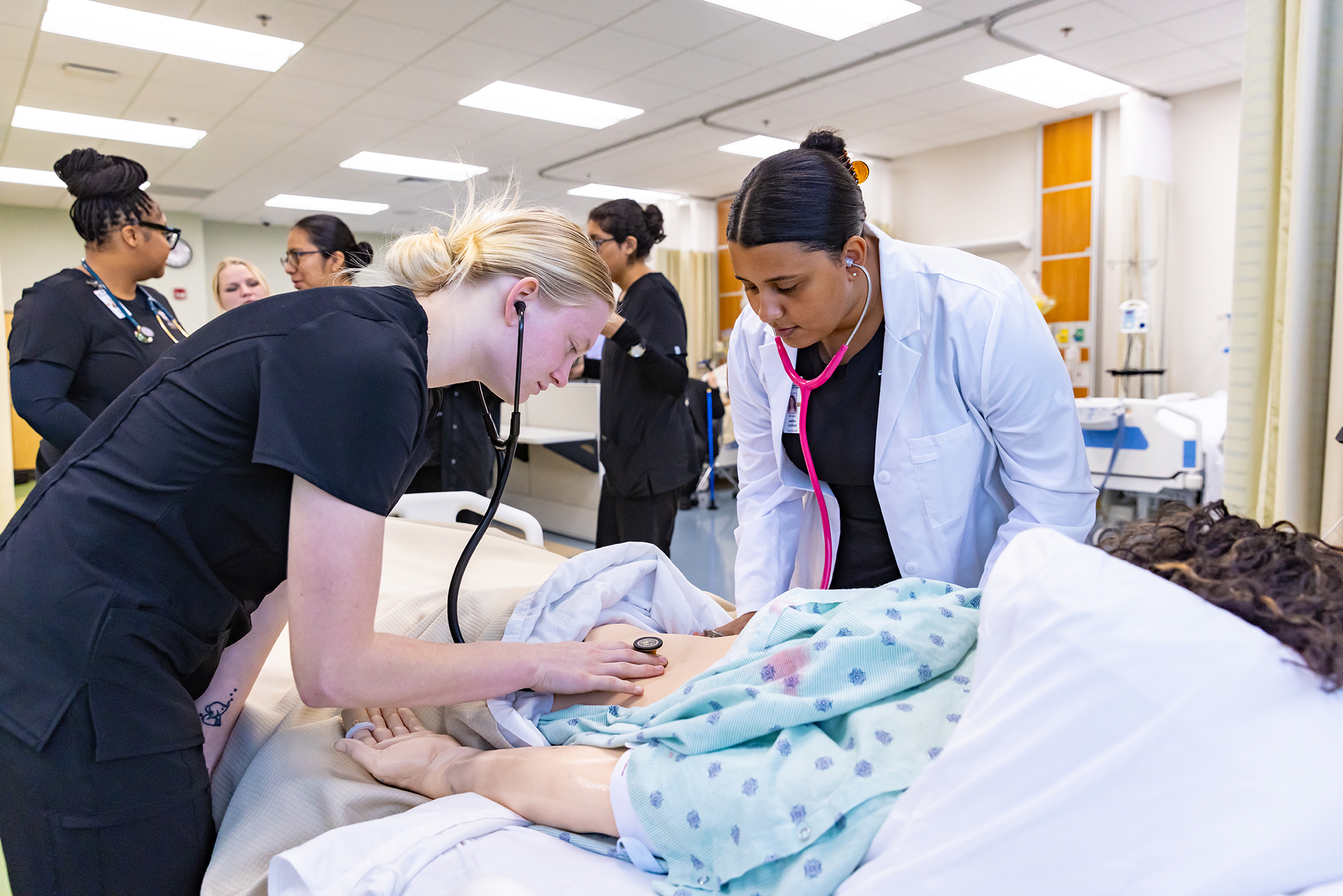 Two nursing students listen for heartsounds on a patient