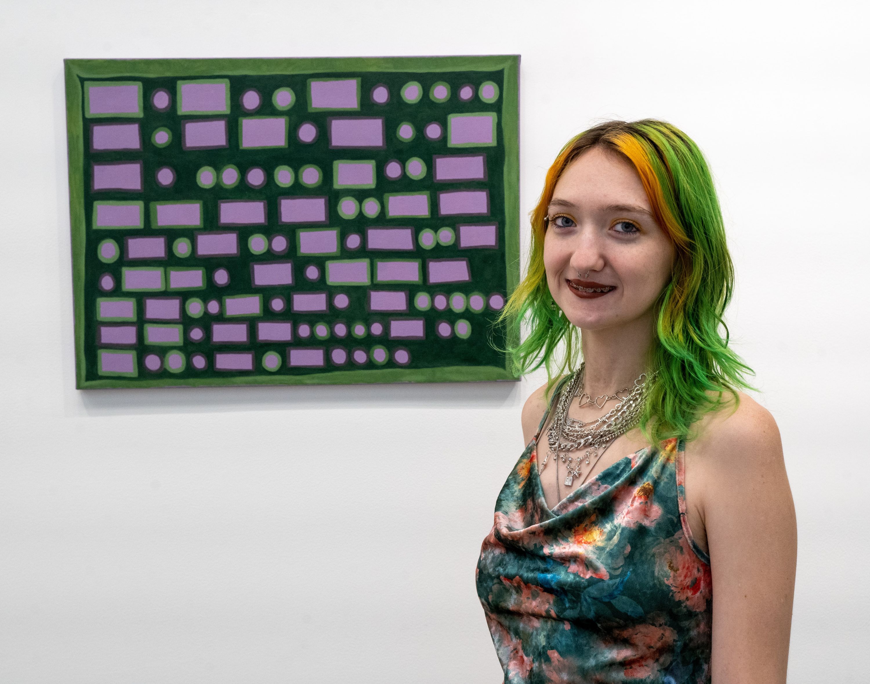 Art student, Bethani Paul, at the reception for the senior art exhibition, Hidden Lives. Art student, Bethani Paul, at the reception for the senior art exhibition, Hidden Lives. She's wearing a colorful dress, posing for the camera in front of her painting of morse code.