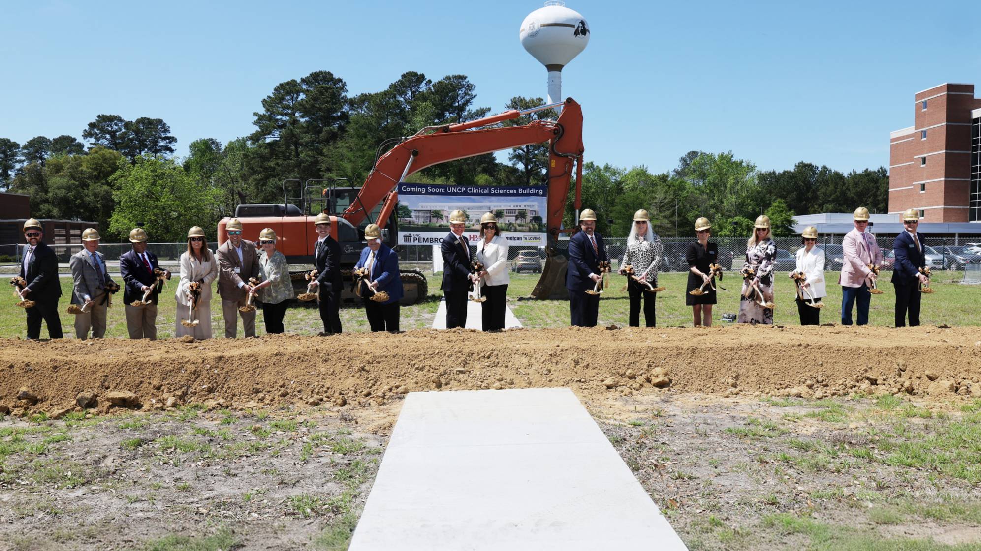 A group of community and university leaders holding shovels and wearing hardhats at the groundbreaking for the Clinical Sciences Building on the campus of UNCP.