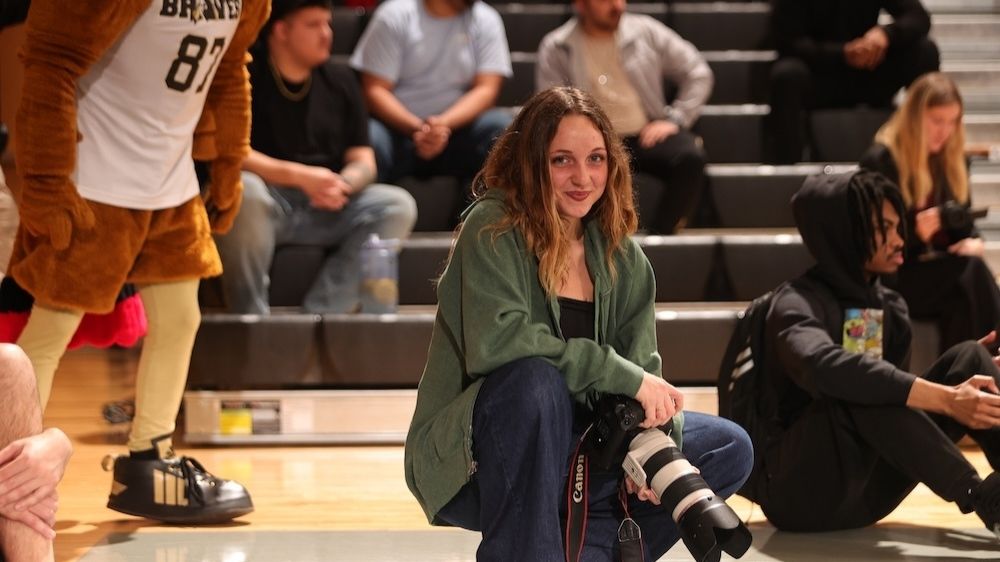 Michela Gritti kneels courtside at basketball game while holding a camera