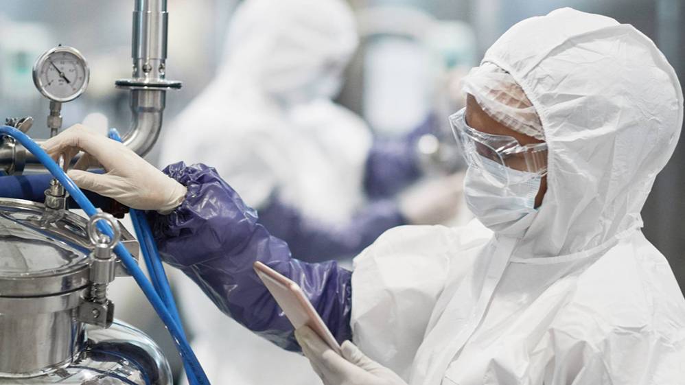 A technician in full protective cleanroom gear operates biopharmaceutical manufacturing equipment, representing the hands-on lab training offered through UNCP