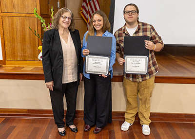 Michela Gritti and Sean Hancock in front of stage holding their awards with Dr. Darlene Natale