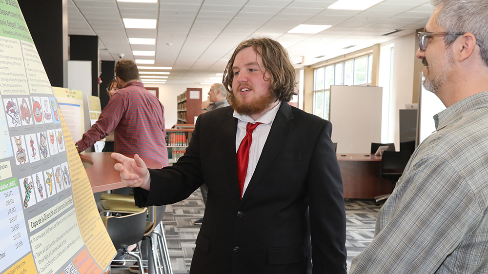 UNCP REACH Fellow Christopher Green stands with his research presentation at UNC Pembroke