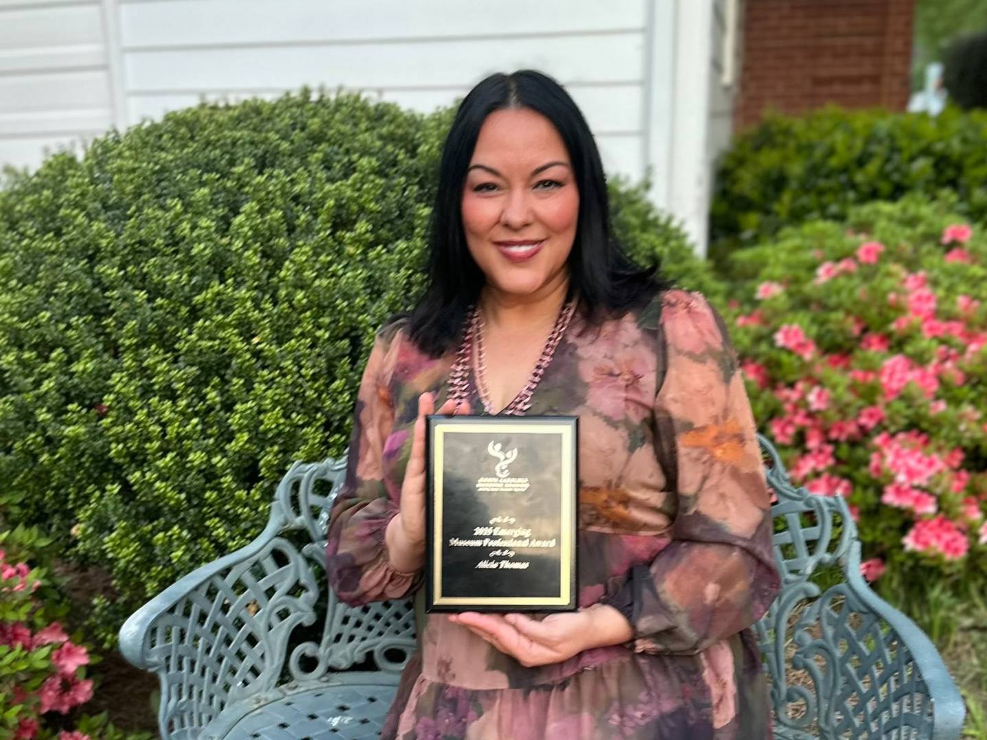 Alicia Thomas sitting on a bench shows off her museum award