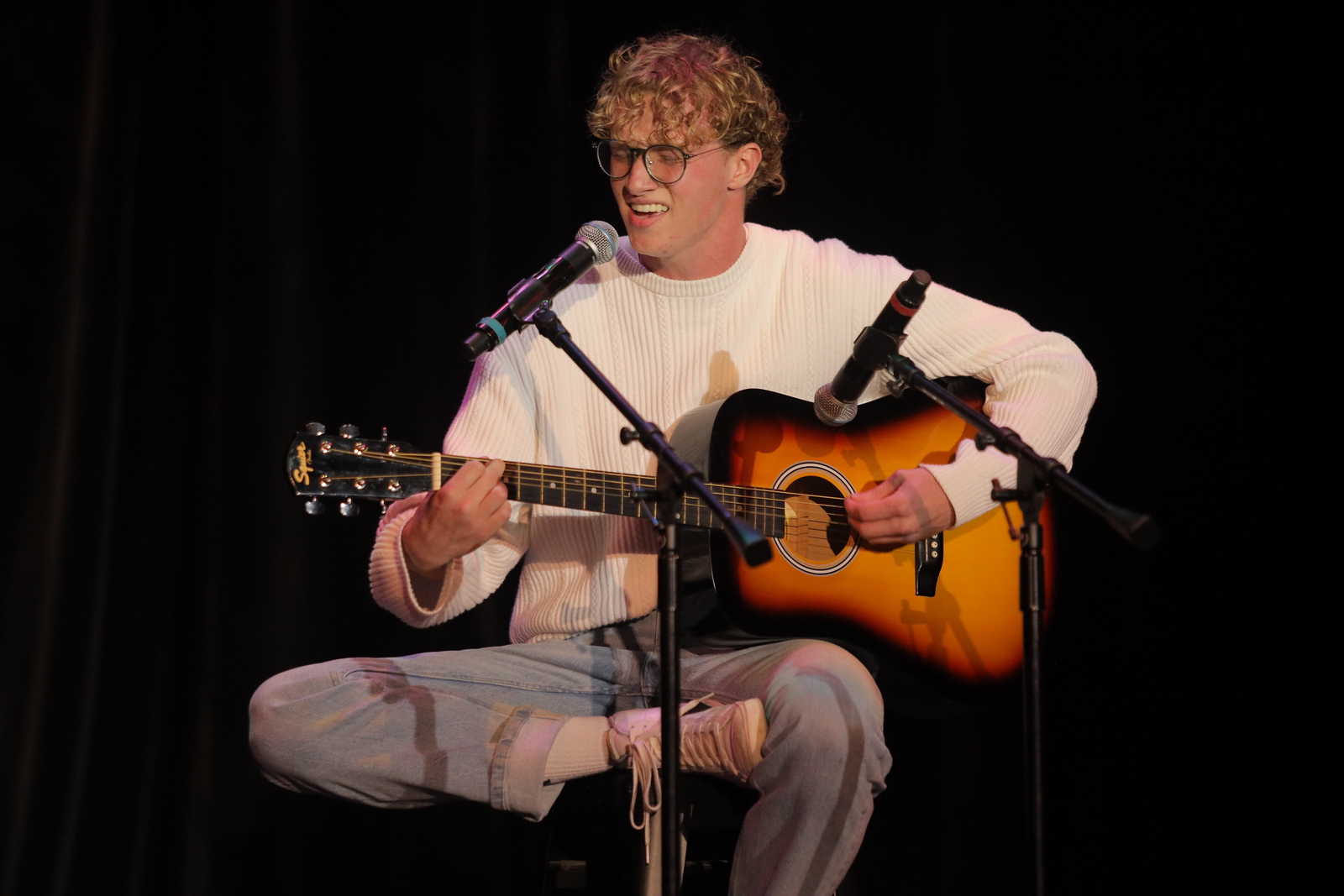 Student performing on stage while singing and playing acoustic guitar at UNC Pembroke, highlighting student in the performing arts.