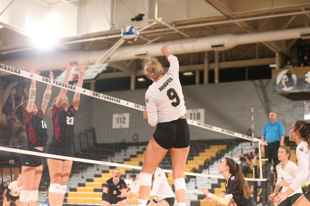 Woman wearing number 9 jersey is midair spiking a volleyball over the net.