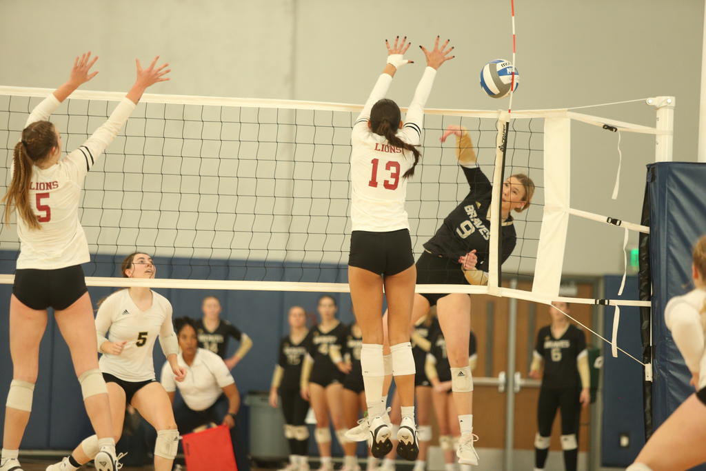 A woman wearing a number 13 jersey is jumping to block a volleyball being hit.