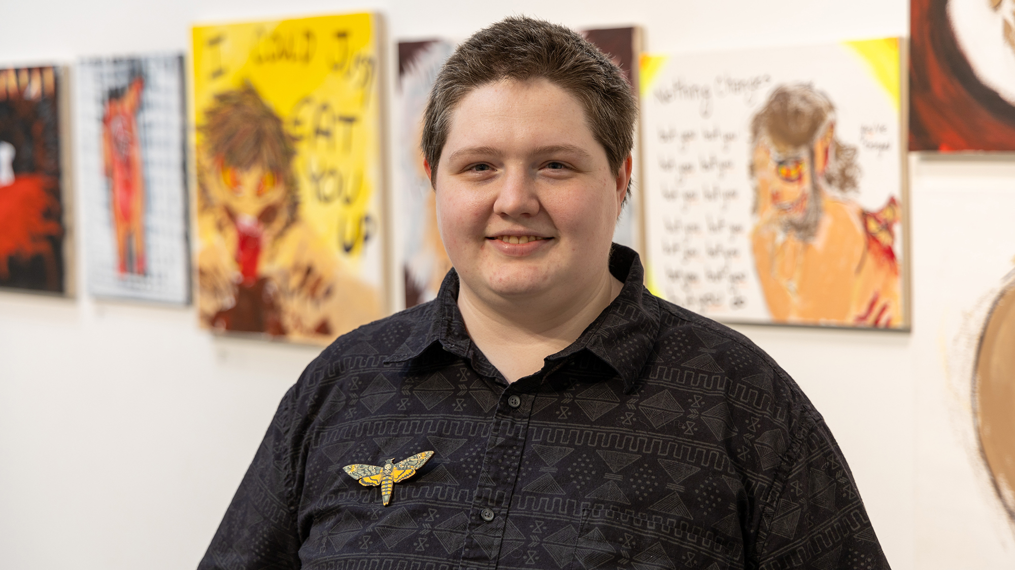 art student smiling with many paintings hanging on the wall behind him