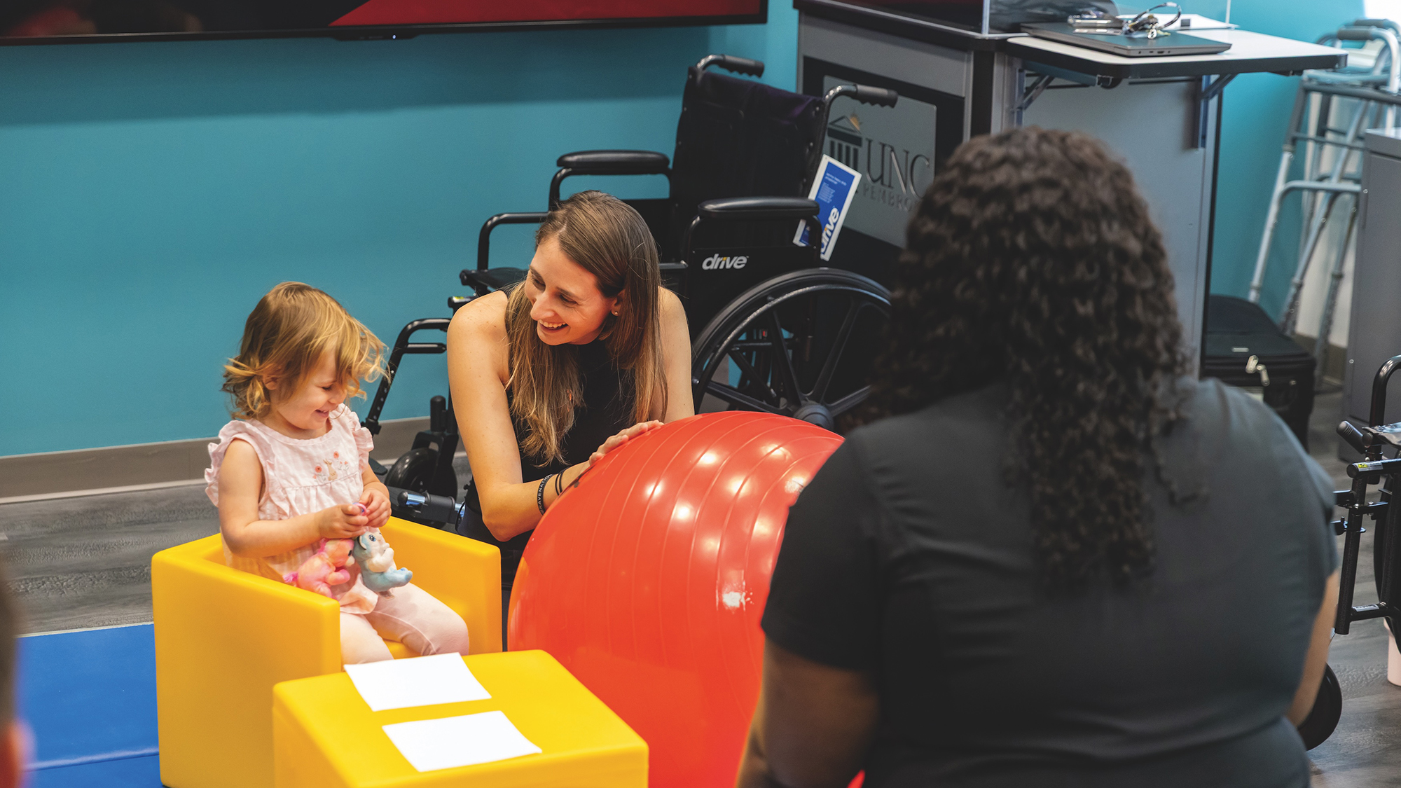mother distracting daughter with toys while healthcare student looks on