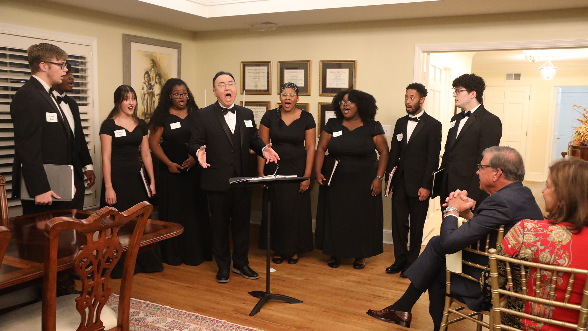 male student takes lead on vocals in front of formally dressed singers for the chancellor and his wife seated in front
