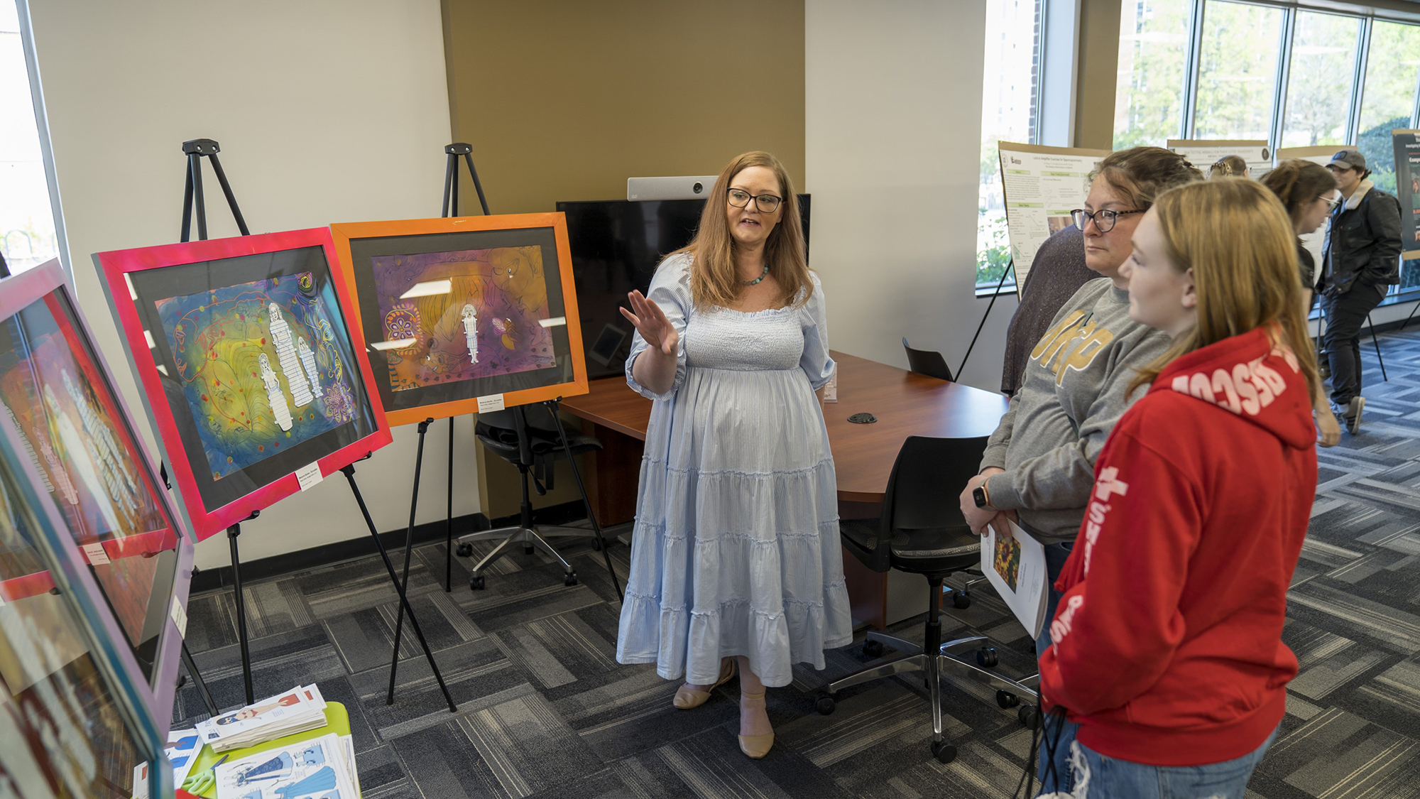 Female art student presenting her work, four paintings, to attendees to the undergraduate research symposium at UNCP.