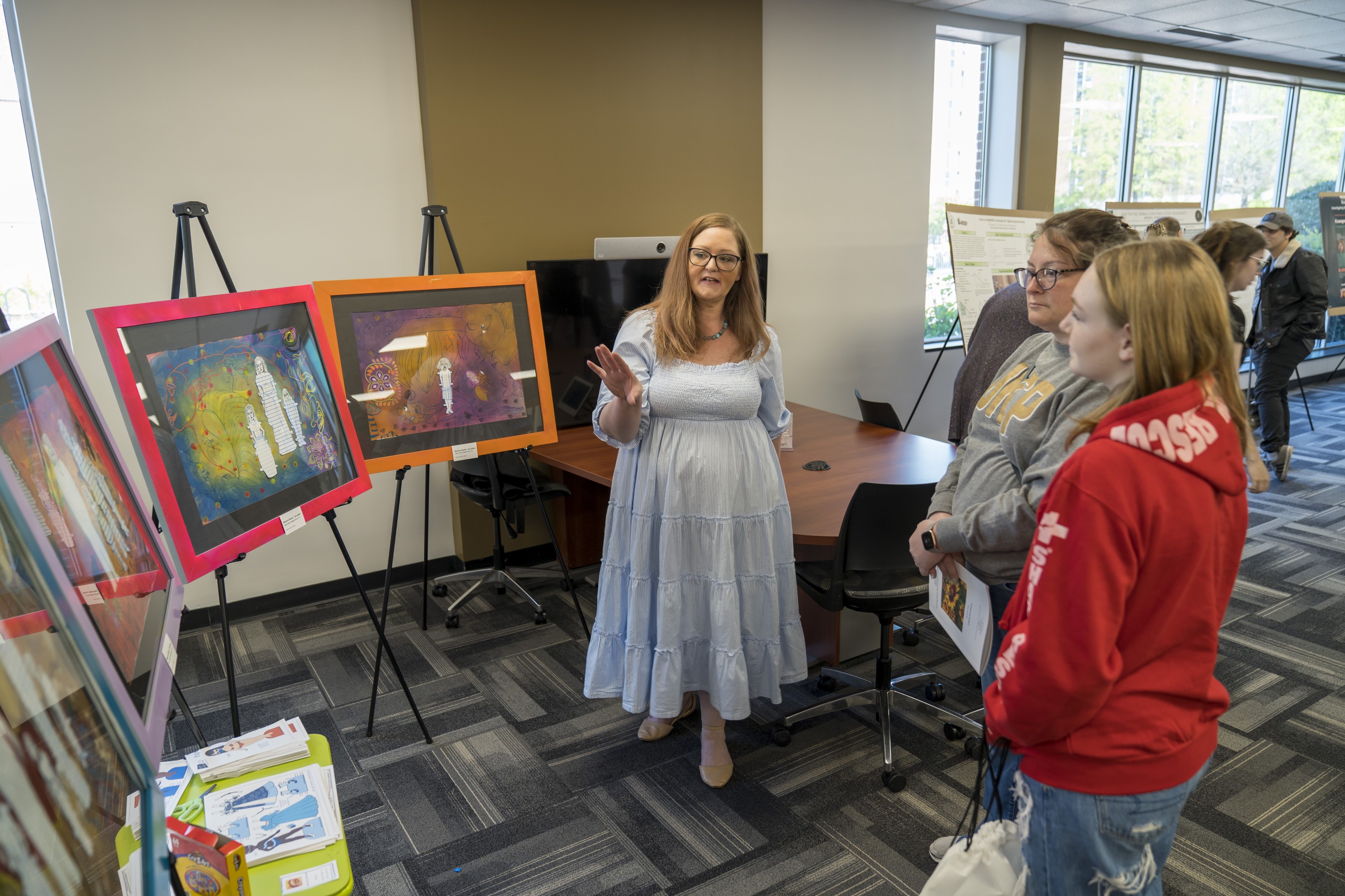 Female art student presenting her work, four paintings, to attendees to the undergraduate research symposium at UNCP.