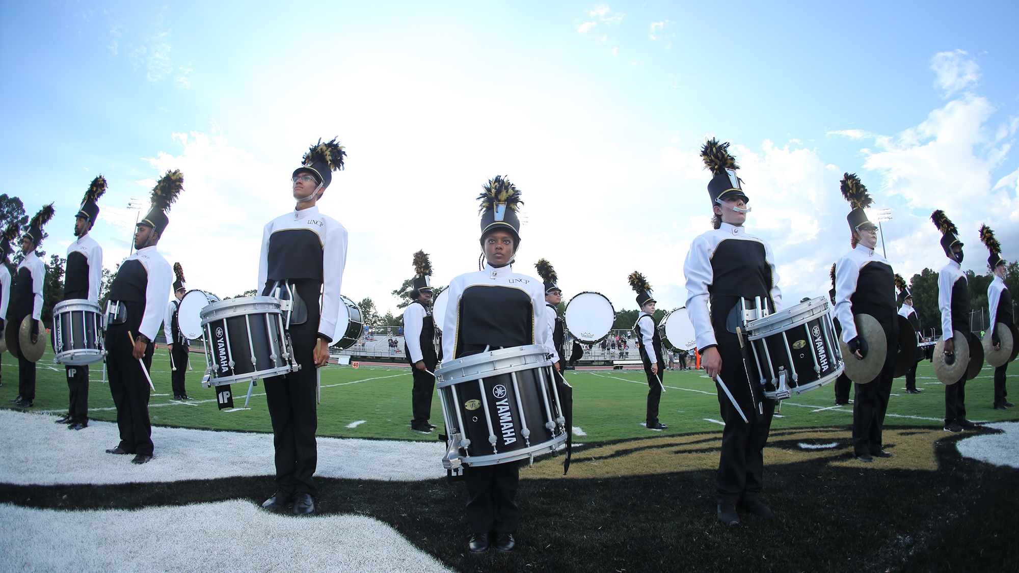fisheye lens picture of drumline performing on the UNCP logo on the football field