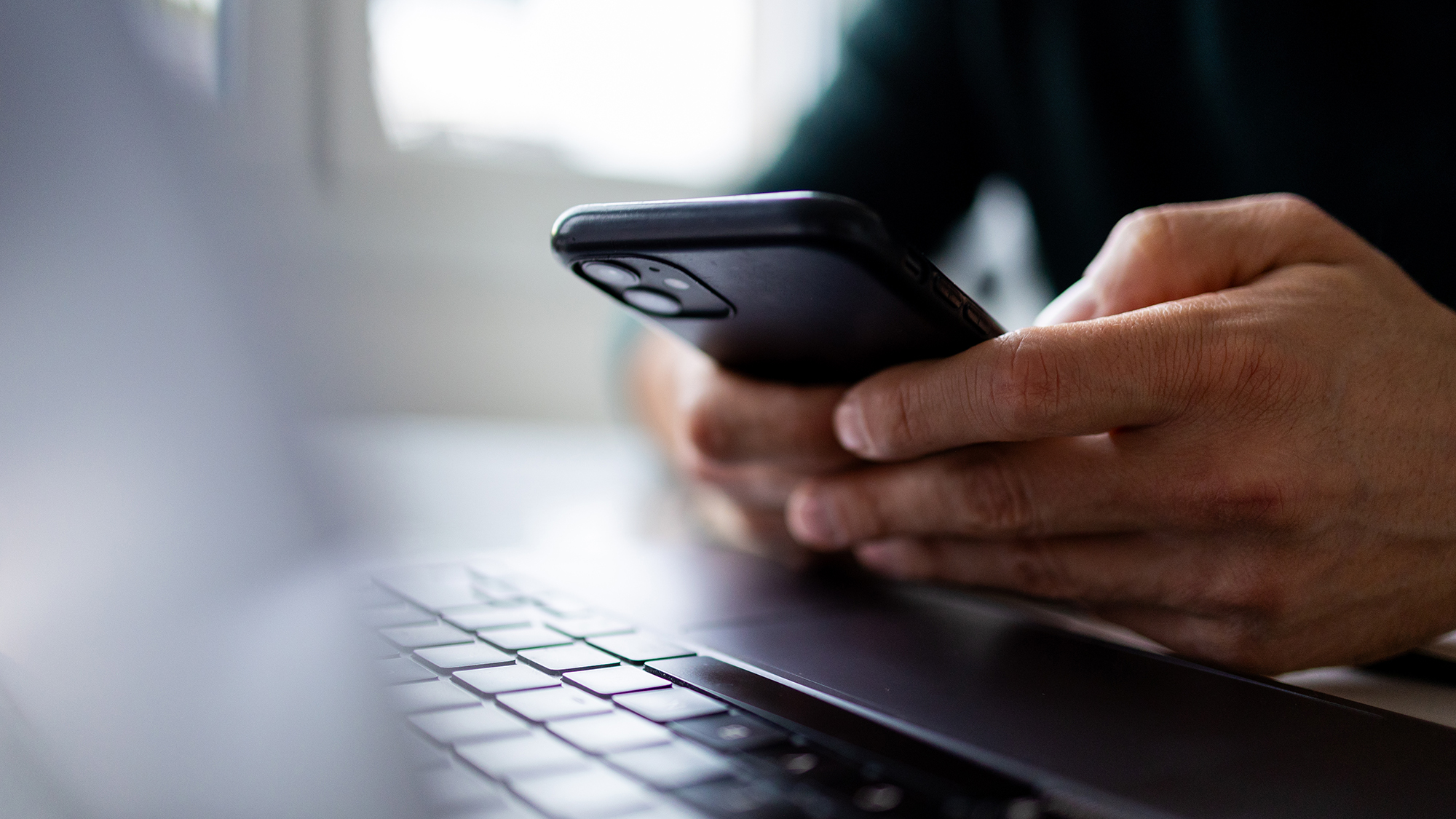 close-up of smartphone in users hand over a keyboard