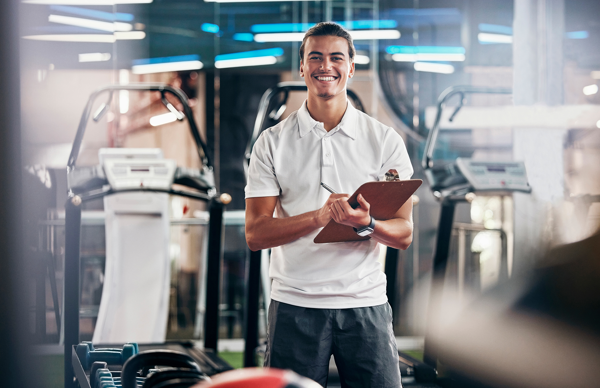 man in gym holding clipboard in front of exercise equipment