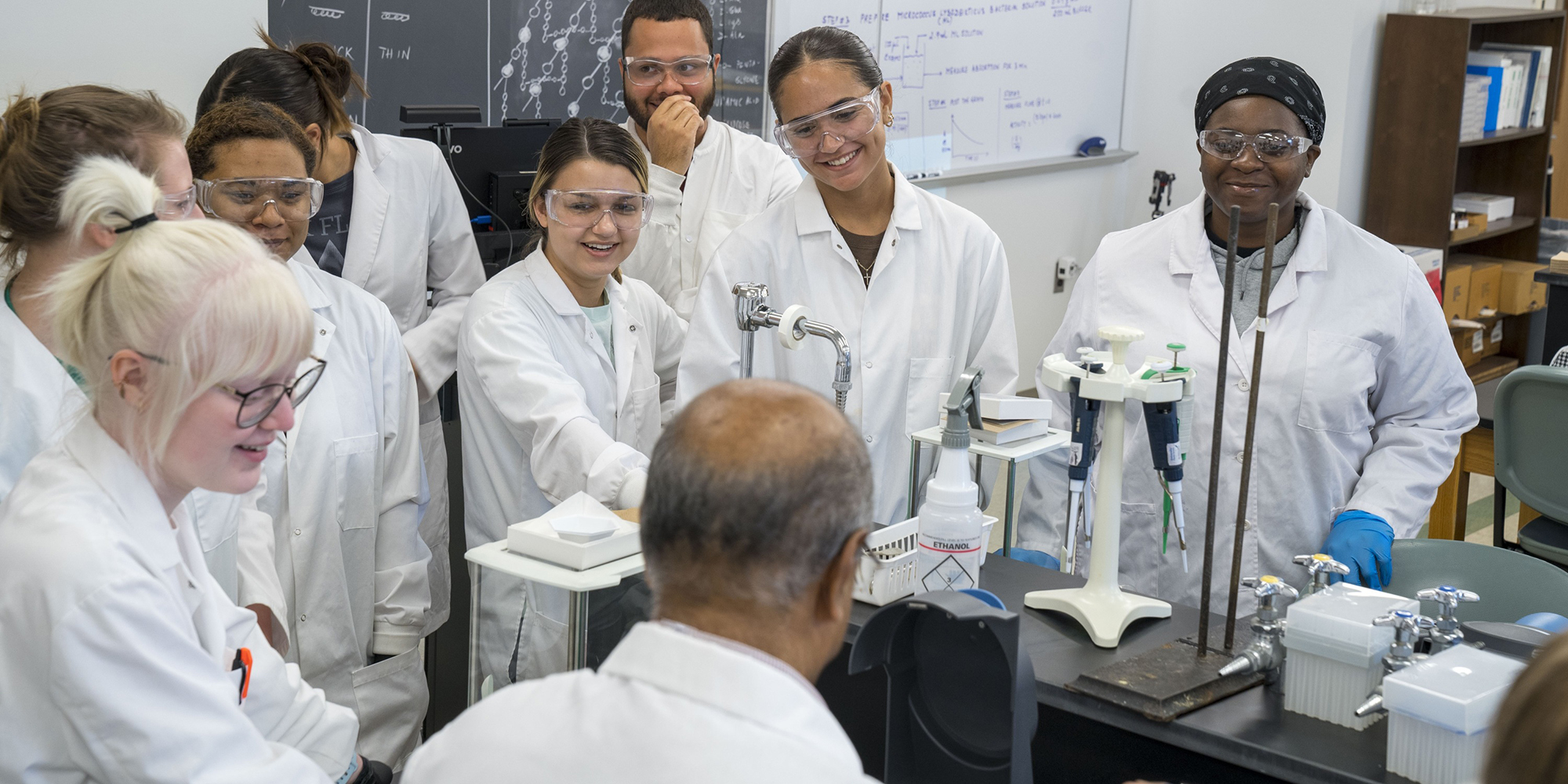 Smiling students in a chemistry lab around the professor who is deomonstrating the lab experiment at UNC Pembroke.