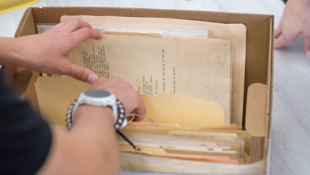 Hands sorting through a cardboard box of historical documents.