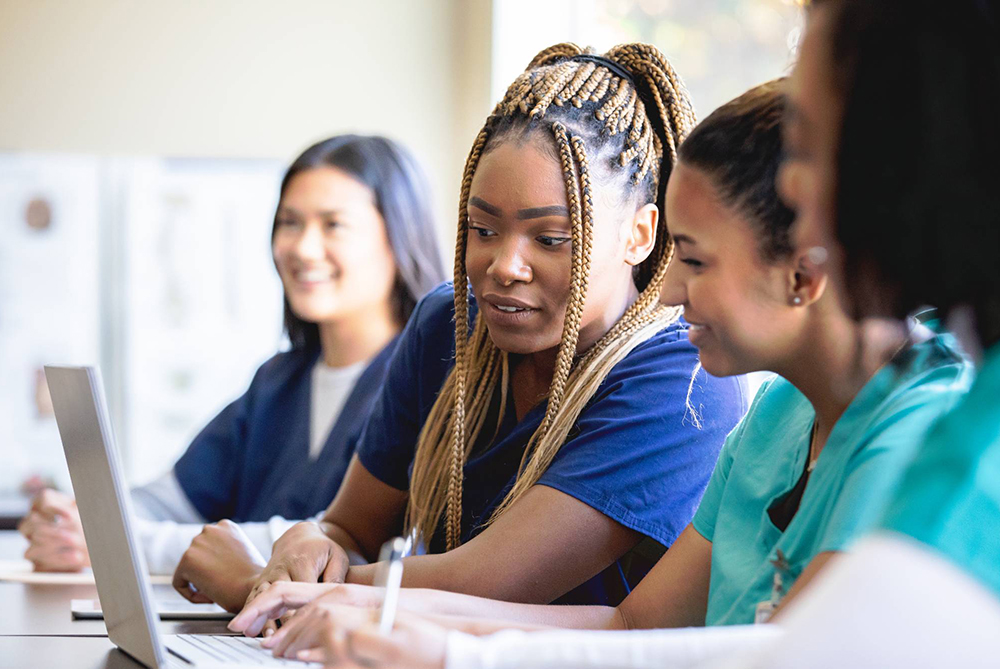 nursing students inside of a classroom looking at a laptop