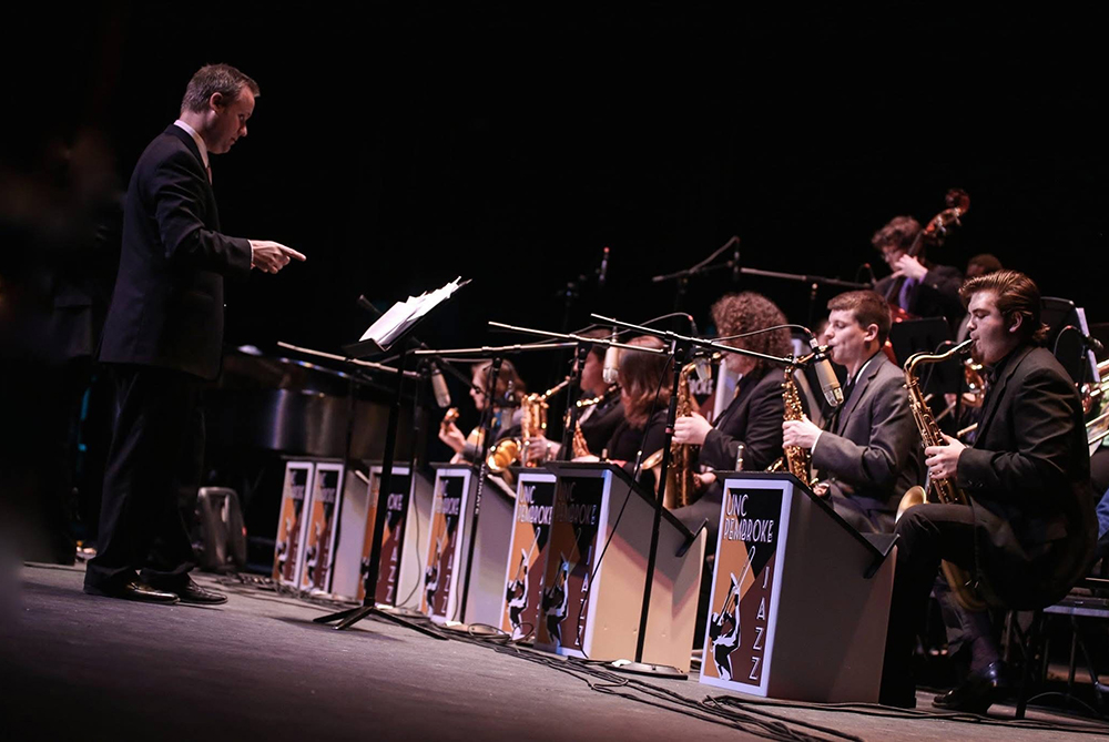 A conductor leads a student concert band during a live performance in a packed auditorium.