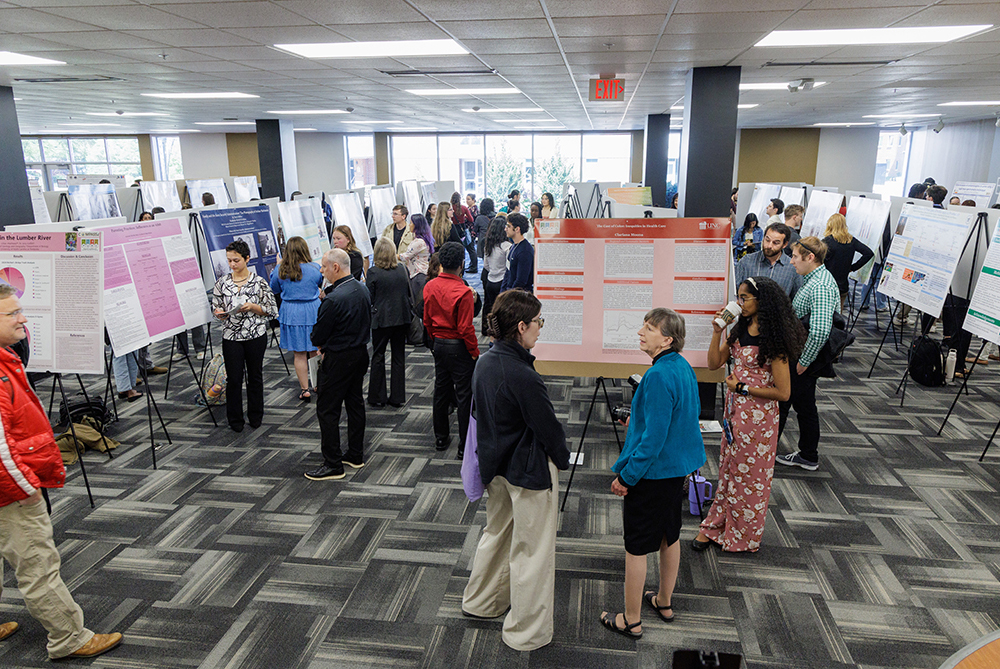 students and faculty walk poster displays at a research symposium on the UNC Pembroke campus