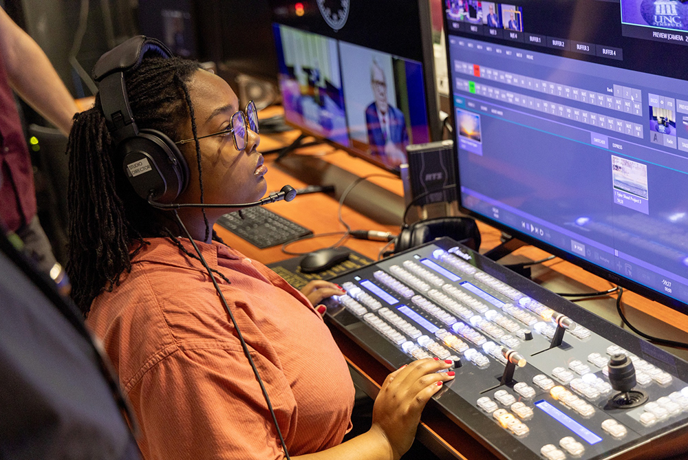 Mass Communications student in the TV studio control room at the control board, switching live cameras for a show.