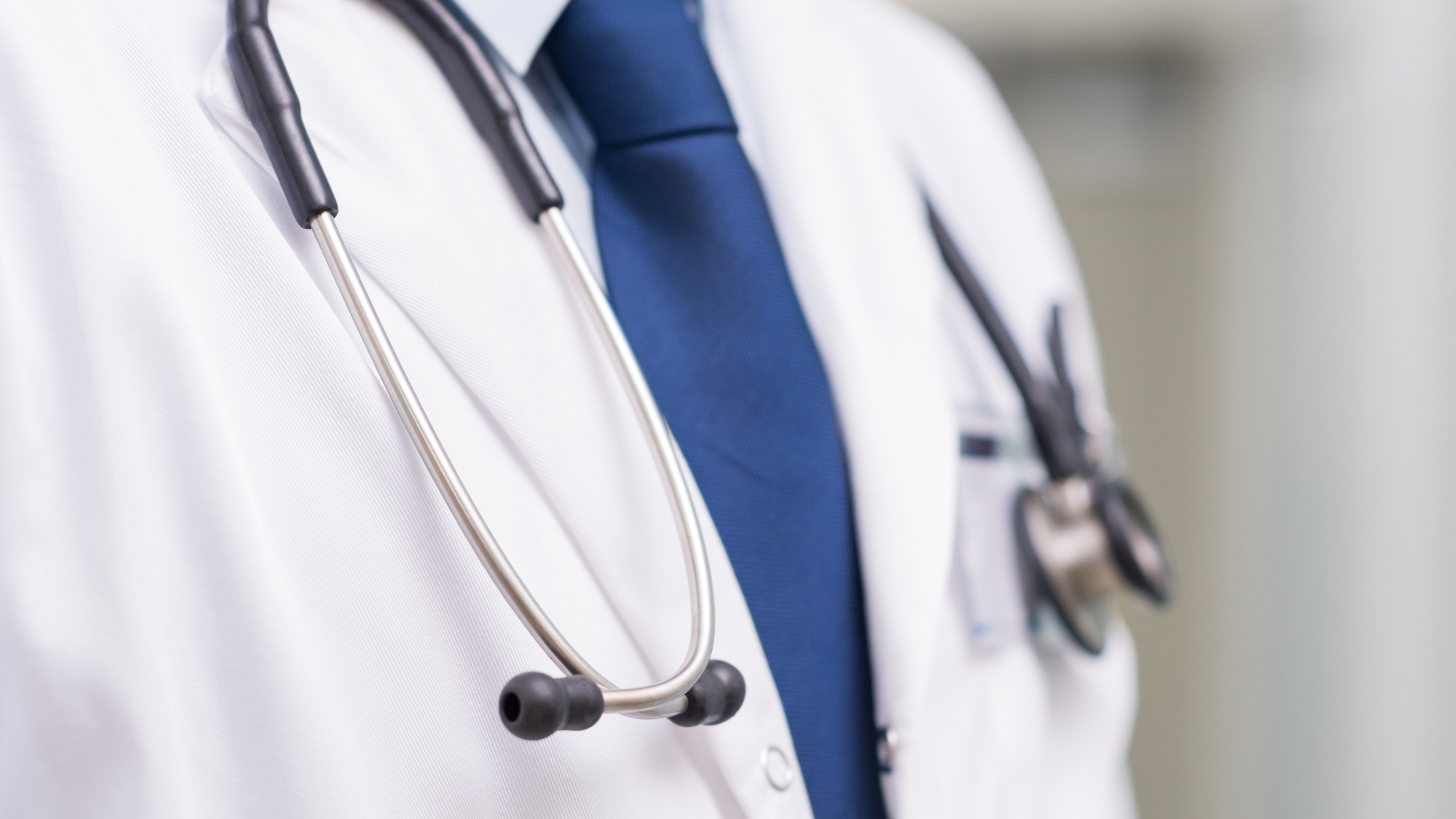 Close-up of a healthcare professional wearing a white coat, blue tie, and stethoscope, symbolizing medical practice, professionalism, and clinical care.