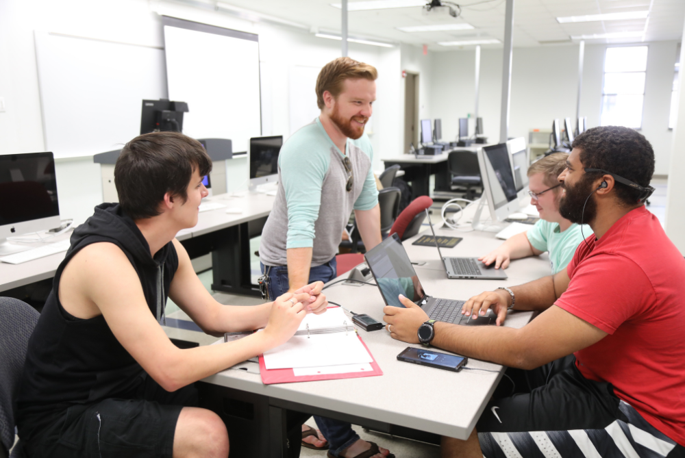Students in a UNCP cybersecurity lap sitting around a computer and talking