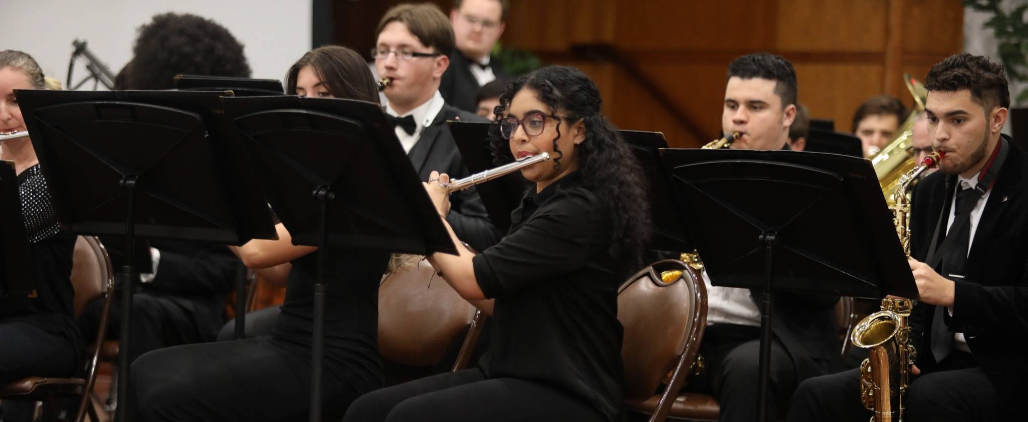 UNC Pembroke jazz ensemble students perform on stage, featuring saxophone, guitar, and percussion players with microphones and music stands branded with "UNC Pembroke Jazz.