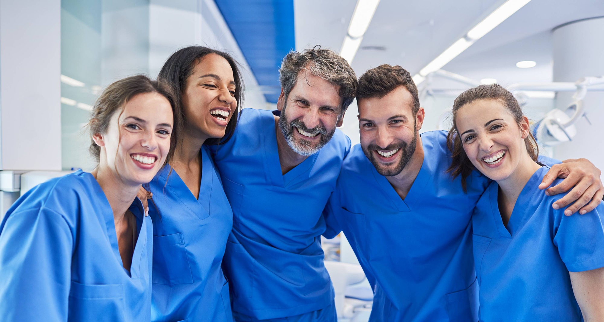 Nurses smiling in a hospital setting with the arms draped over each others shoulders