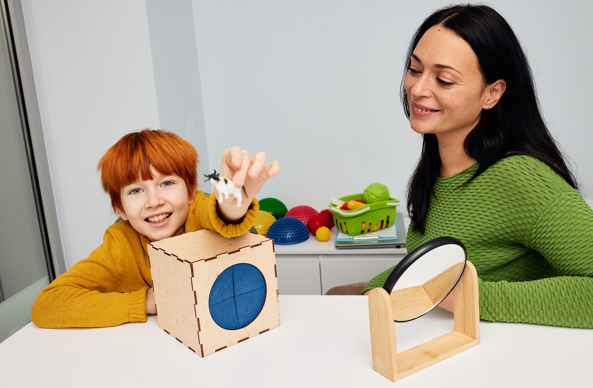 woman in geen sweater watching young boy play with animal shapes and blocks