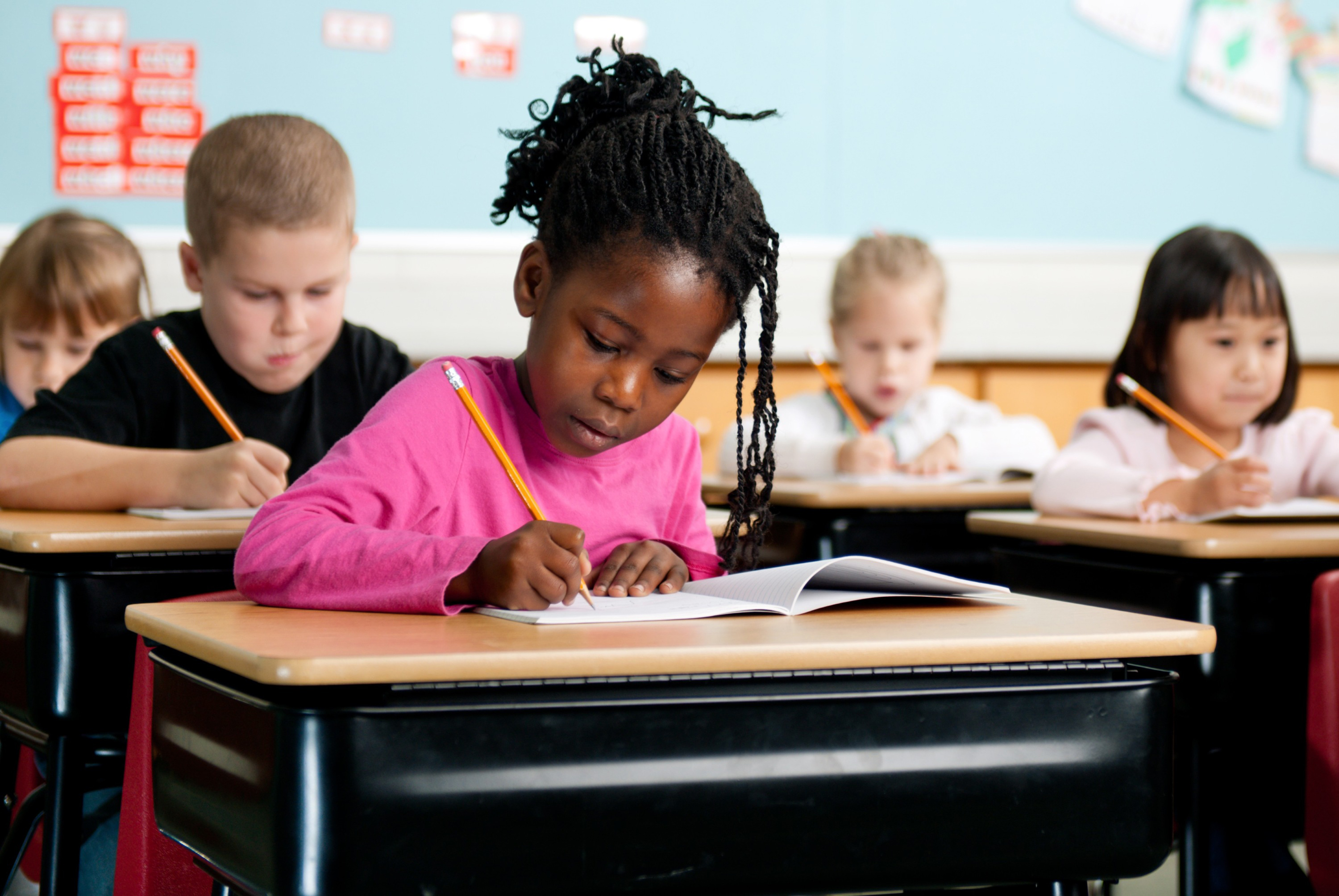 Diverse group of elementary school children at desks in a classroom working in notebooks.
