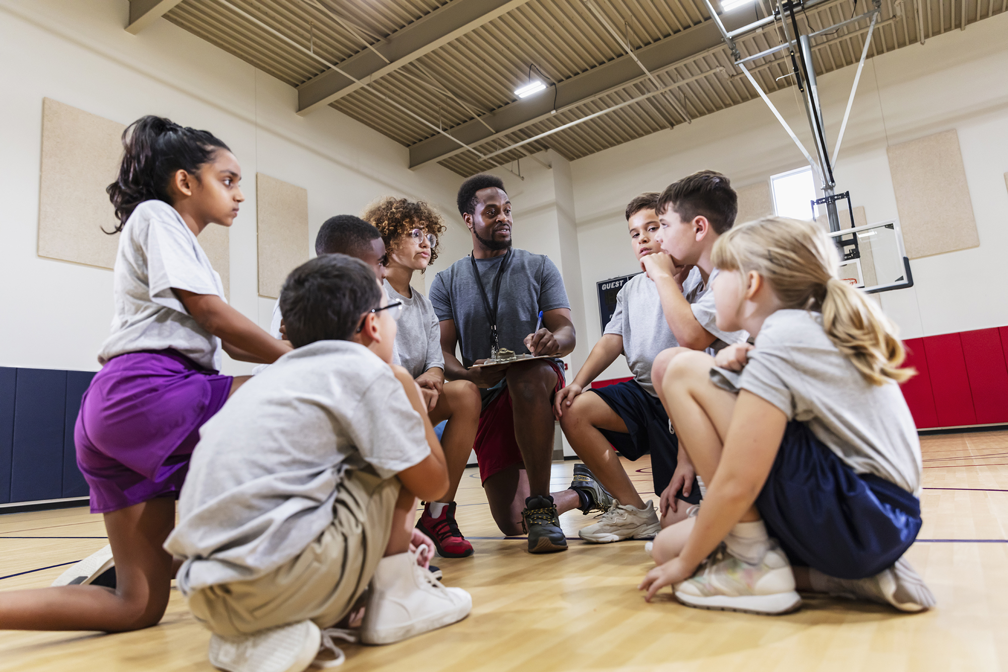 male PE teacher with class of students of basketball court
