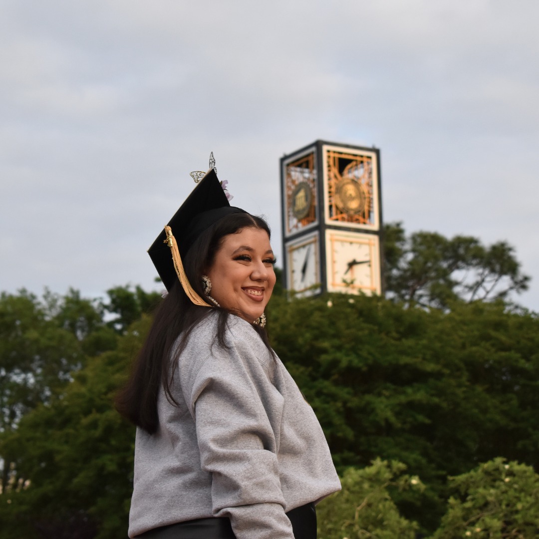 Ashley Arriaga in commencement cap in front of UNCP tower