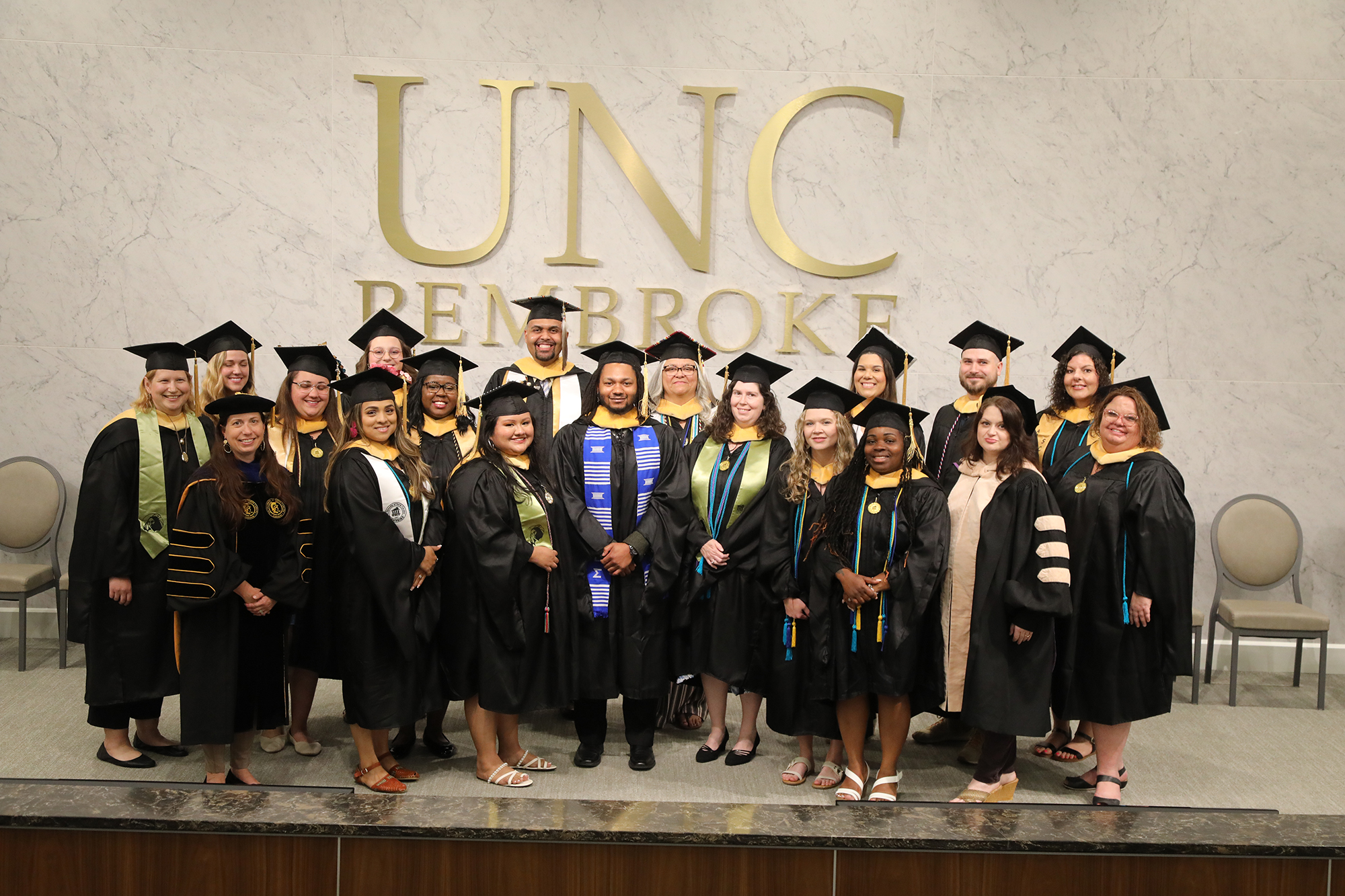 group of UNCP Social Work graduates wearing regalia and posing under a UNC Pembroke sign