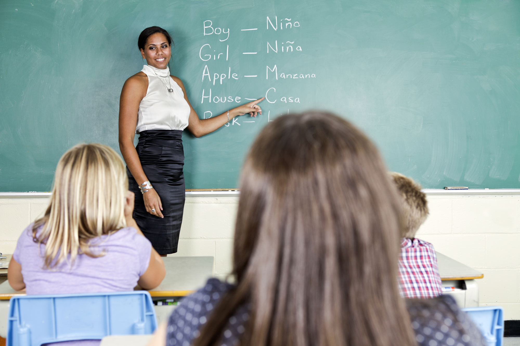 female teacher in front of chalkboard with English and Spanish words written on it