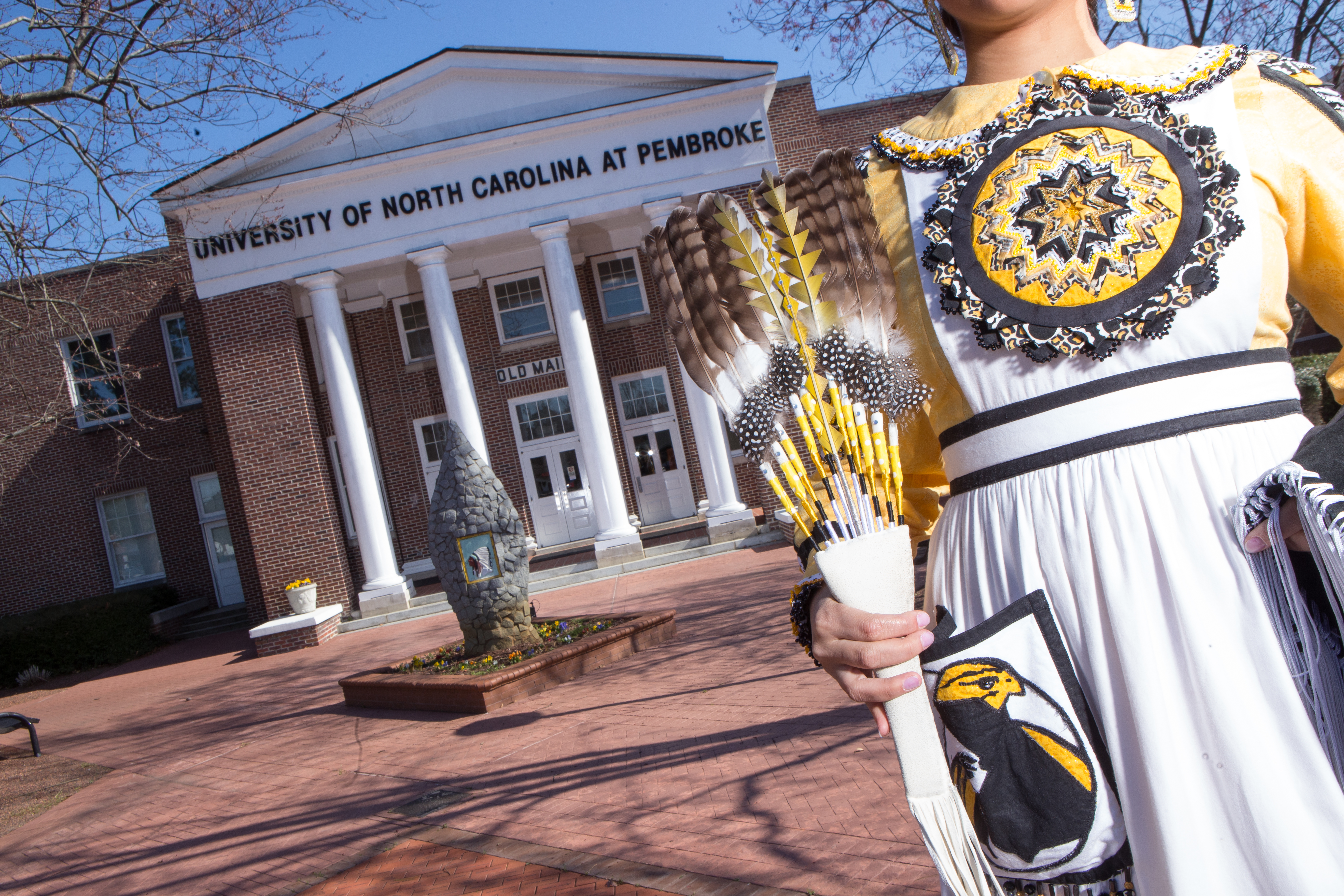 Front of Old Main at UNCP with Lumbee woman in black and yellow regalia in the forefront