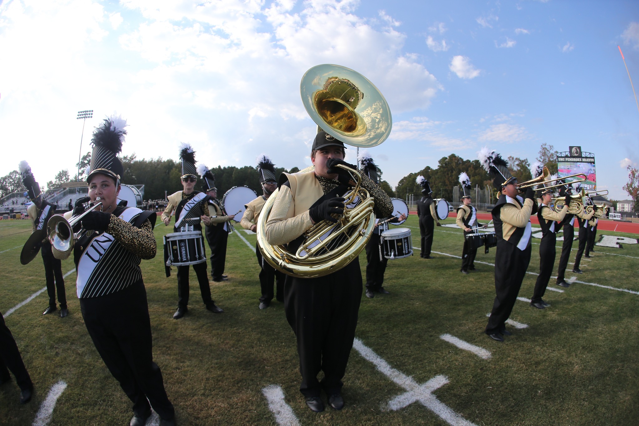 students in marching band uniforms holding instruments on the UNCP football field