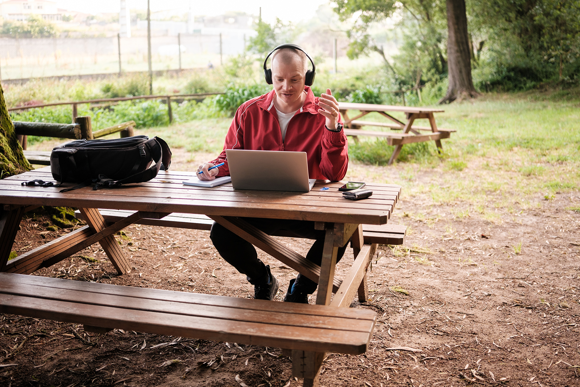 man with headphones and laptop sitting at a picnic table outside