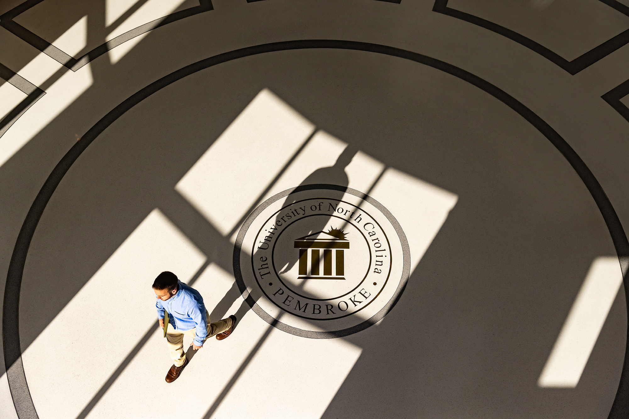 student in blue shirt walkin across the floor of the business college at UNCP