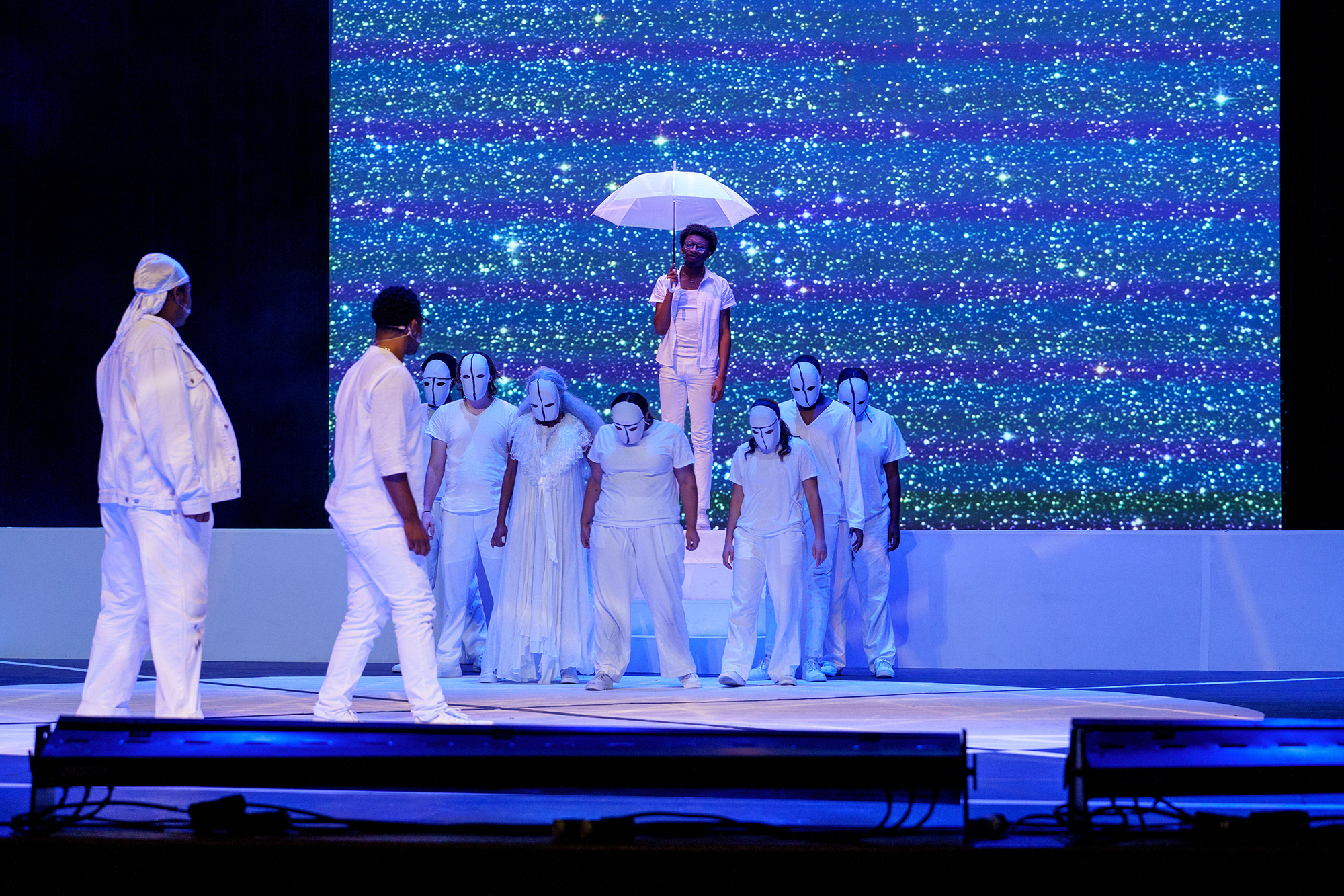 students on stage in white costumes with umbrella
