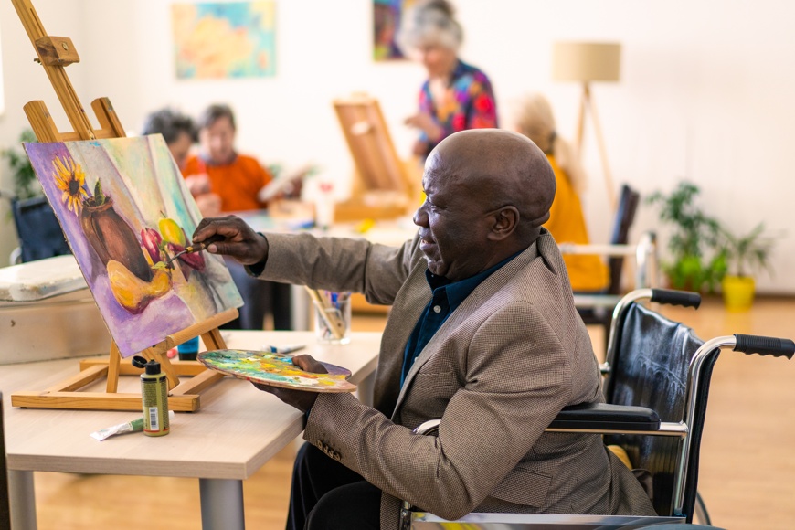 An elderly african american man in a wheelchair painting.
