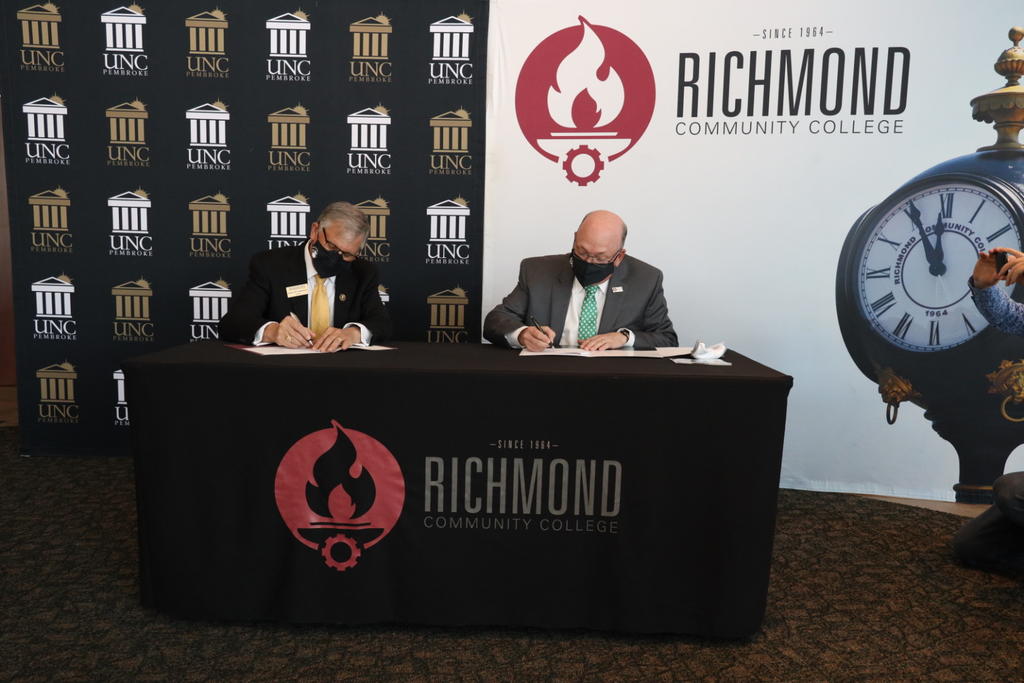 UNCP Chancellor Robin Gary Cummings, left, and RCC President Dale McInnis sign a Growing Your Own partnership during an event at Cole Auditorium on the campus of Richmond Community College