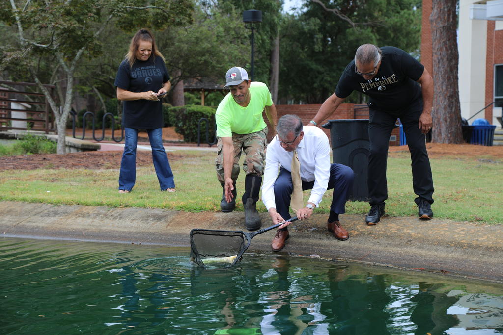 Chancellor Cummings releases Koi int the water feature as Kerry Revels and Harvey and Sheila Godwin look on