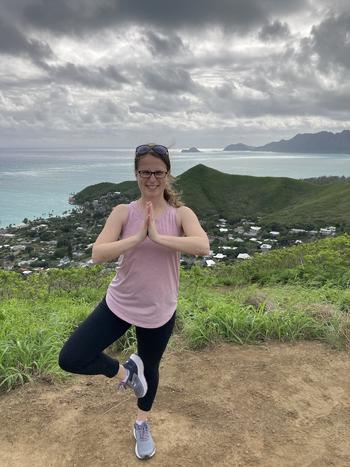 A young woman in a yoga pose on top of a mountain with the ocean in the background